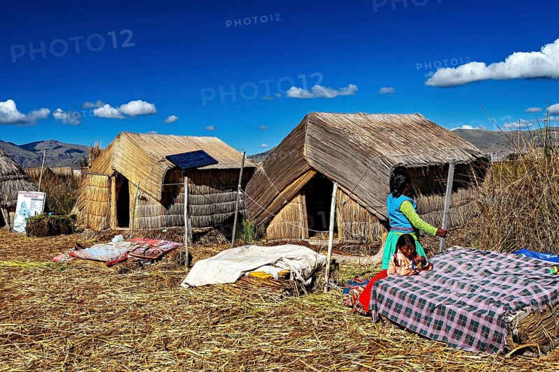 Woman approaches huts made of reeds, dressed in traditional clothing, The floating reed islands of the Uros in Lake Titicaca in Peru