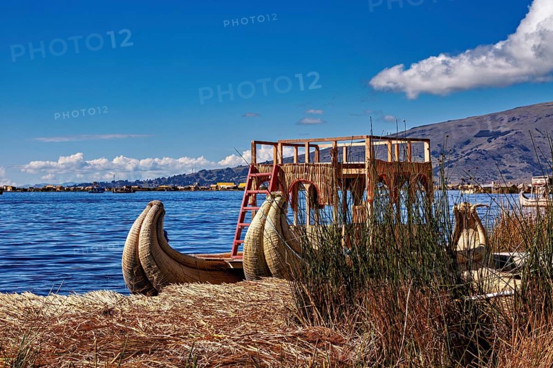 A traditional reed boat is lying on the shores of the lake under a cloudy sky, The floating reed islands of the Uros in Lake Titicaca in Peru