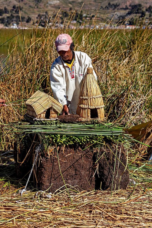Man showing a model of straw huts and figures on a natural surface, The floating reed islands of the Uros in Lake Titicaca in Peru
