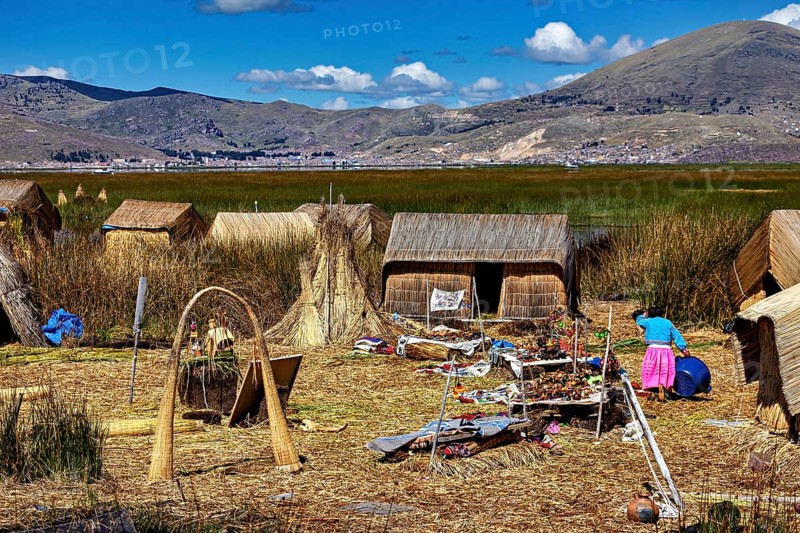 Reed huts with mountains in the background and scattered crafts, The floating reed islands of the Uros in Lake Titicaca in Peru