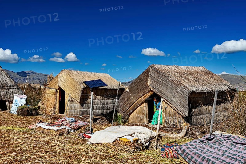 Several reed huts with solar panels under a blue lakeside sky, The floating reed islands of the Uros in Lake Titicaca in Peru