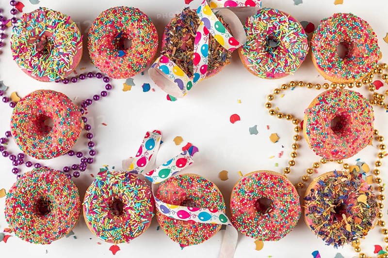 Donuts with sprinkles and confetti surrounded by streamers and strings of pearls on a bright background