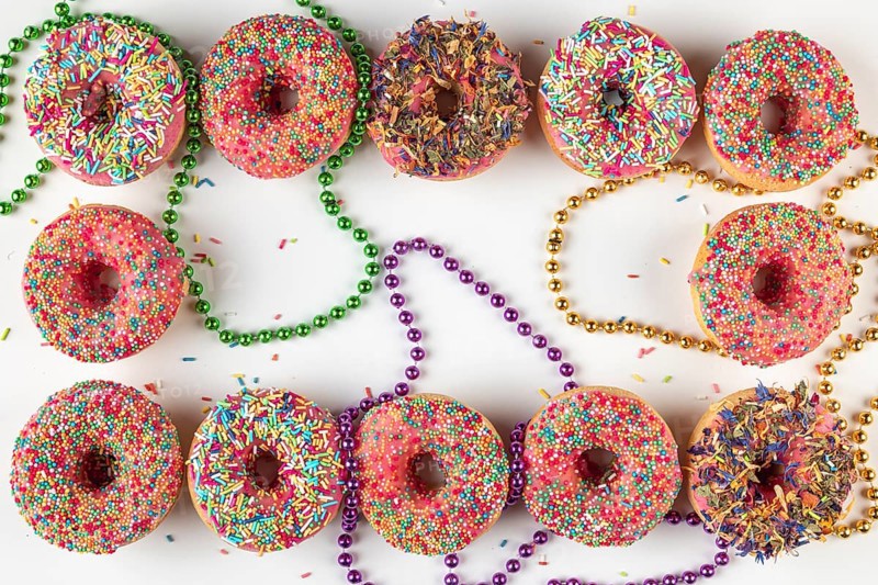 Donuts with colorful icing and sprinkles surrounded by colored pearl necklaces on a white background