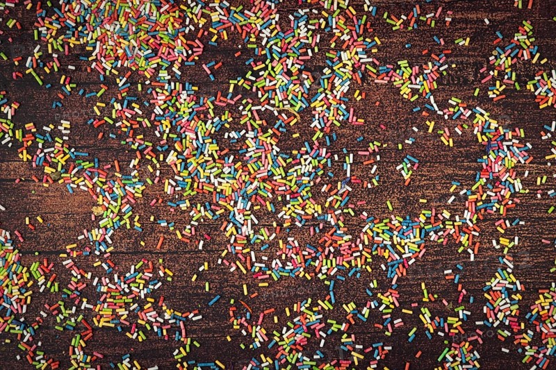 Colourful sprinkles scattered on dark wooden table