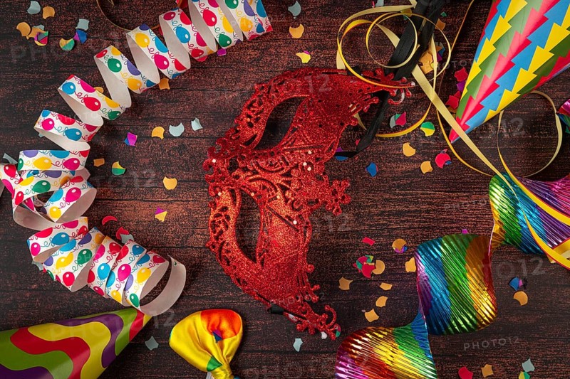 Red mask surrounded by party decorations such as streamers and confetti on table, carnival