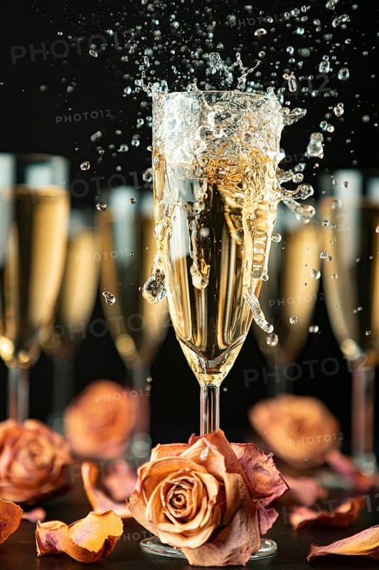 Sparkling wine made of glass surrounded by other glasses and rose petals on a black background