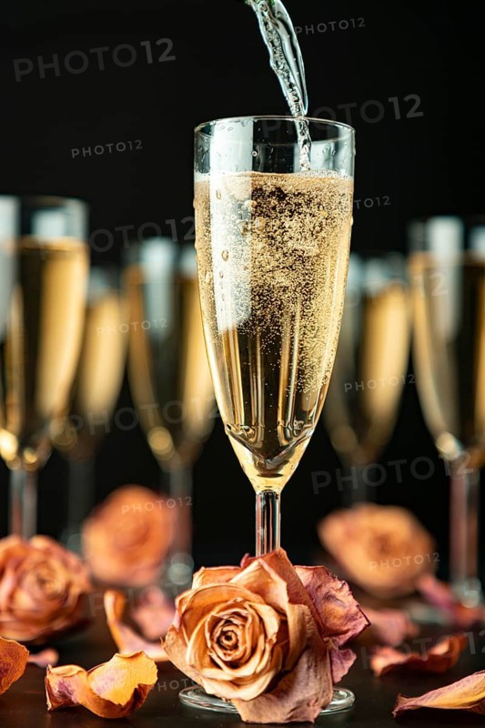 Sparkling wine is being poured, champagne glasses with rose petals on a black background