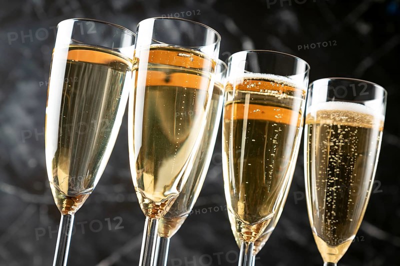 Filled champagne glasses with foaming contents against a dark background