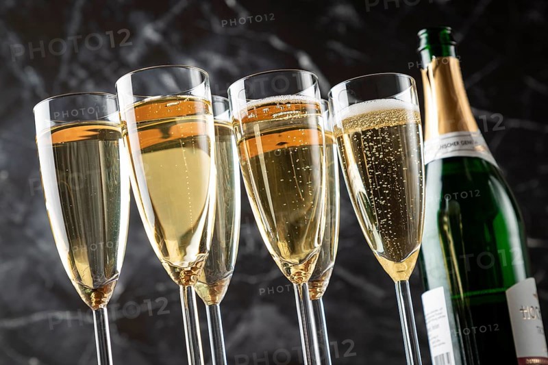 Six glasses filled with sparkling wine and an open champagne bottle against a black background