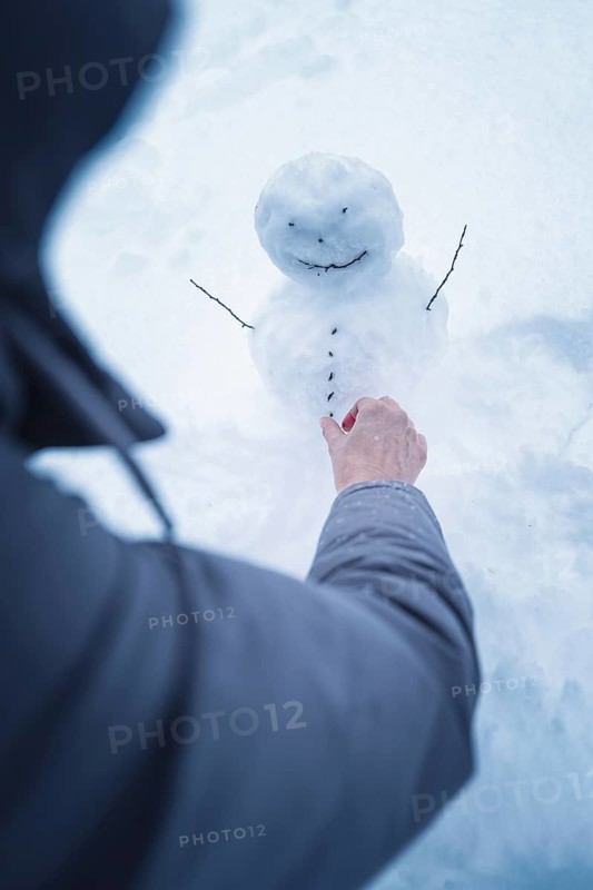 A person builds a small snowman surrounded by snow, broom field, Black Forest, Germany