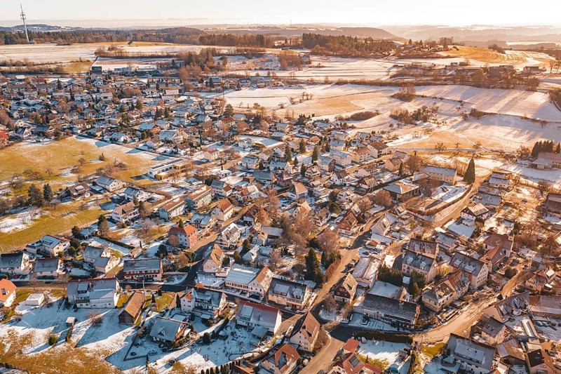 Wide settlement in winter with snow-covered roofs and fields in sunlight from an aerial perspective, Hallwangen, Freudenstadt district, Germany