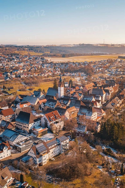 Aerial view of a town with church in the center, surrounded by buildings and winter landscape under blue sky and sunshine, Dornstetten, Freudenstadt district, Germany