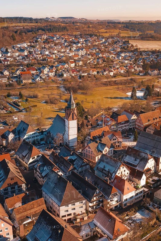 Aerial view focusing on church surrounded by city buildings in a wintry environment in sunlight, Dornstetten, Freudenstadt district, Germany