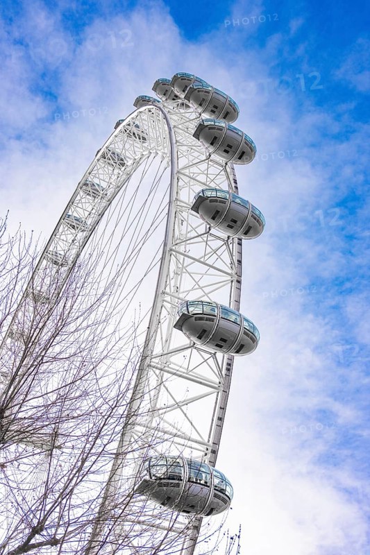 A large Ferris wheel juts into the blue sky surrounded by clouds, London Eye, London, United Kingdom