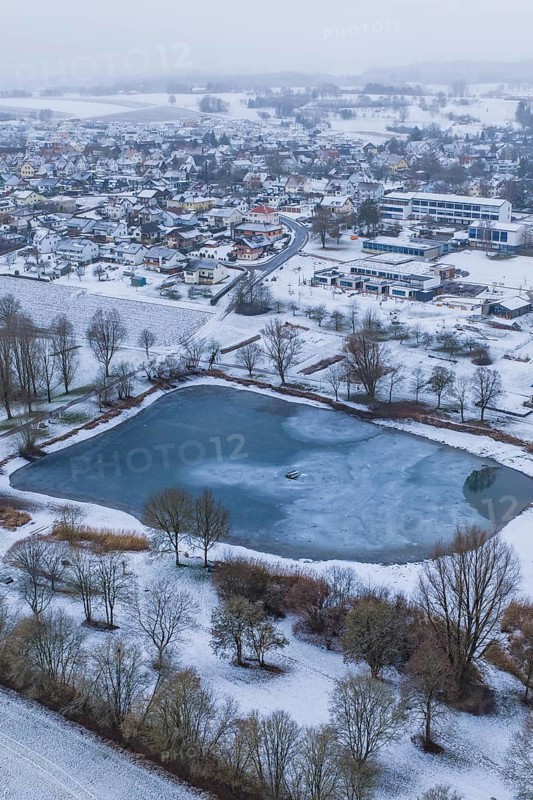 Snowy village with frozen lake seen from above on a grey day, Empfingen, Freudenstadt district, Germany