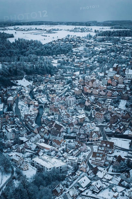 A snow-covered city from the air with many houses and a river, surrounded by hills and forests in a wintry atmosphere, Altensteig, Calw district, Germany