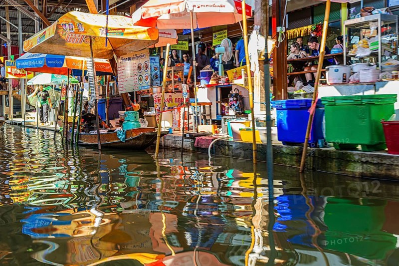 Wooden boat and umbrellas are reflected on the Damneon Saduak floating market channel near Bangkok, Ratchaburi District, Thailand