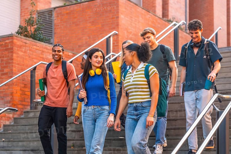 Diverse group of smiling university students walking down outdoor stairs on campus together, carrying books and backpacks, representing education and happiness
