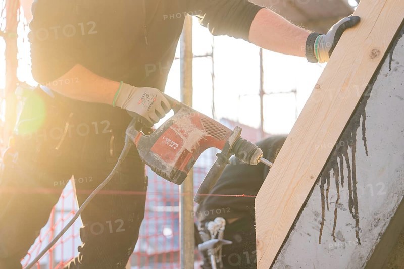 Worker with drill in sunlight working on wood on construction site, carpentry construction, roof extension, renovation, Stuttgart, Germany