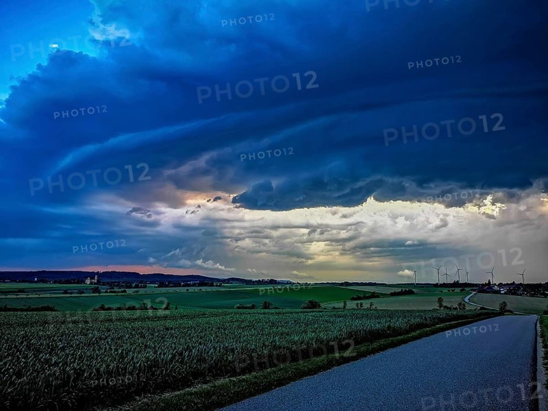 Supercell, approaching thunderstorm with impressive and threatening cloud formation, a thunderstorm over a country road and a village with wind turbines in the background, Baden-Württemberg, Germany
