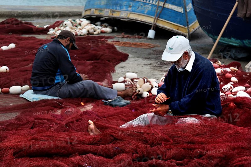 Fishermen repair nets in harbor surrounded by blue boats and tools, Essaouira, Marrakesh-Safi, Morocco