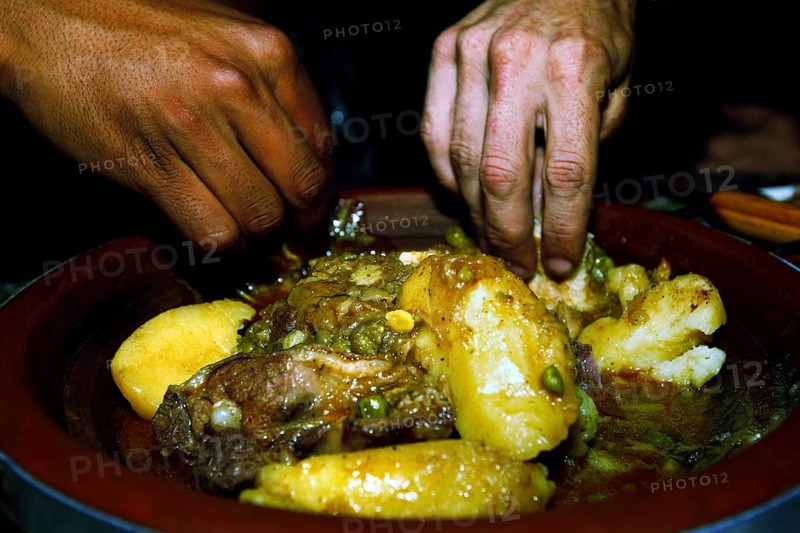Hands serving a traditional Moroccan dish with lamb and potatoes for dinner, Errachidia, Morocco