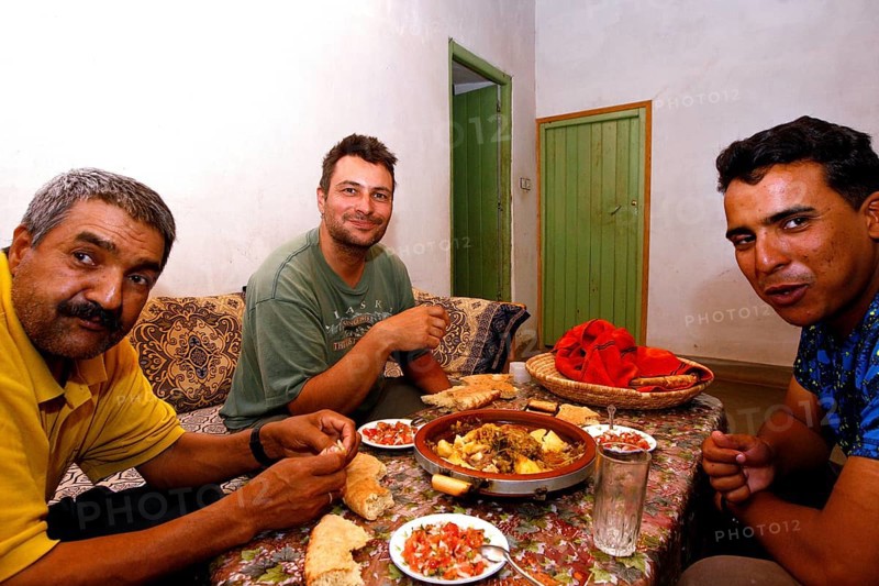 Three men enjoy a Moroccan dinner together with bread and a hearty dish, Errachidia, Morocco