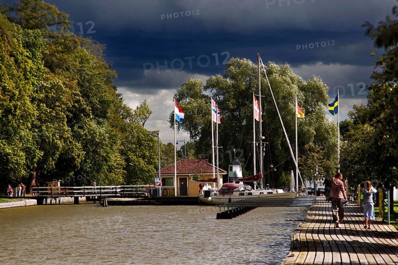 Söderköping harbour on Göta Canal with flags and trees under a cloudy sky, Söderköping, Sweden