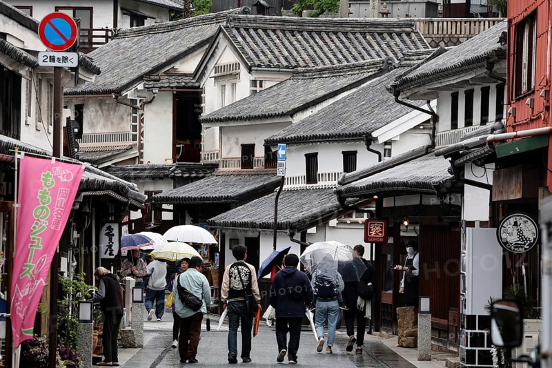 People with umbrellas walk through a historic street with traditional buildings in Kurashiki, Kurashiki, Okayama, Japan