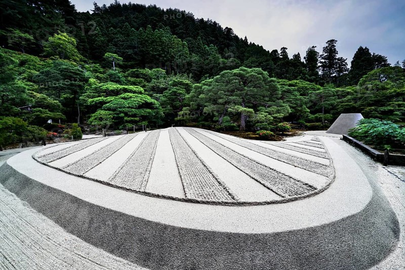 Zen garden of Ginkaku-ji Temple with precise sand patterns and rocks surrounded by green landscape, Kyoto, Japan