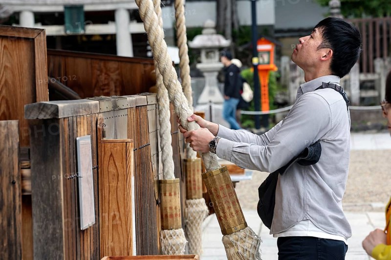 Man pulls a heavy rope to pray at a shrine, Kyoto, Higashiyama, Japan