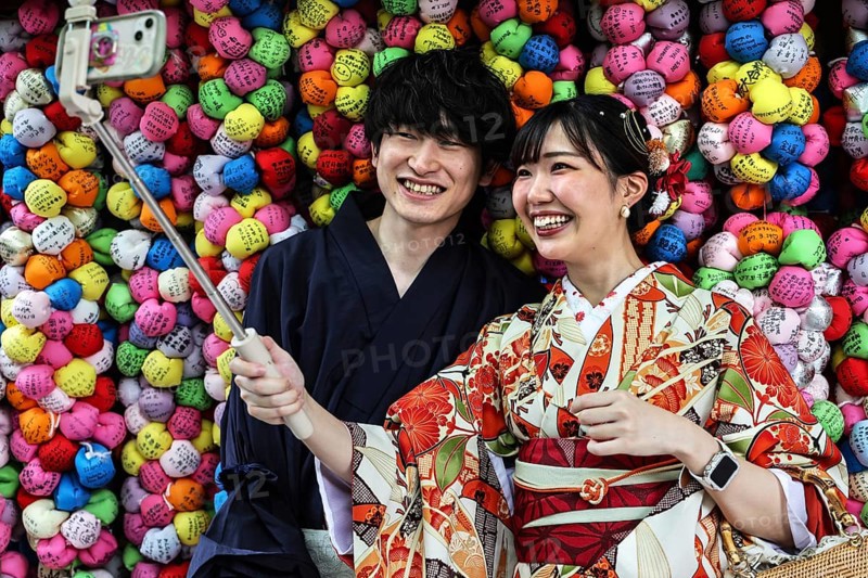 Couple wearing kimonos taking selfies in front of colorful backgrounds at Yasaka Koshindo Temple, Kyoto, Higashiyama, Japan