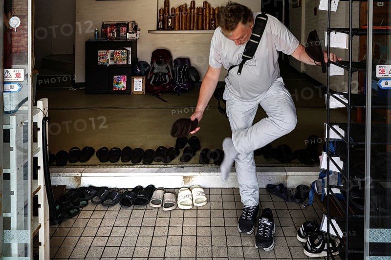 Man changes shoes at the entrance of a Japanese hotel. Traditional practices in hotel lobby, Beppu, Oita, Japan