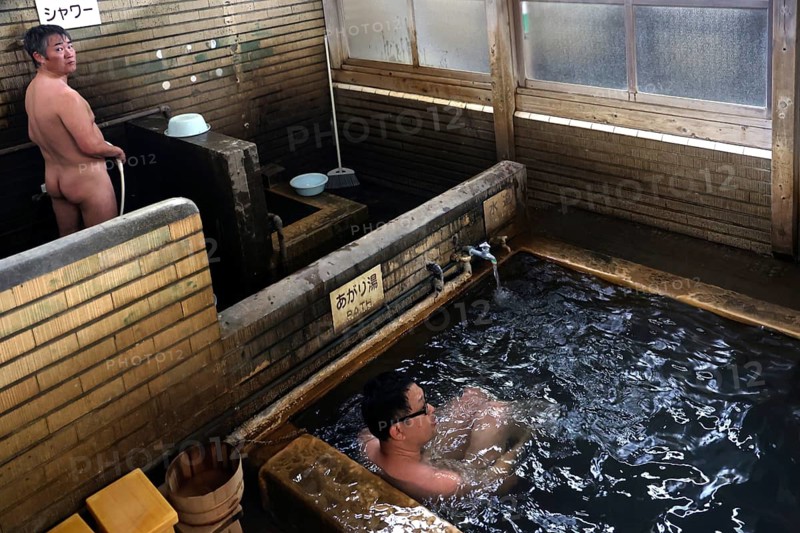 Traditional Japanese onsen bath with wooden walls in a warm setting. People enjoy the relaxing atmosphere, Beppu, Oita, Japan