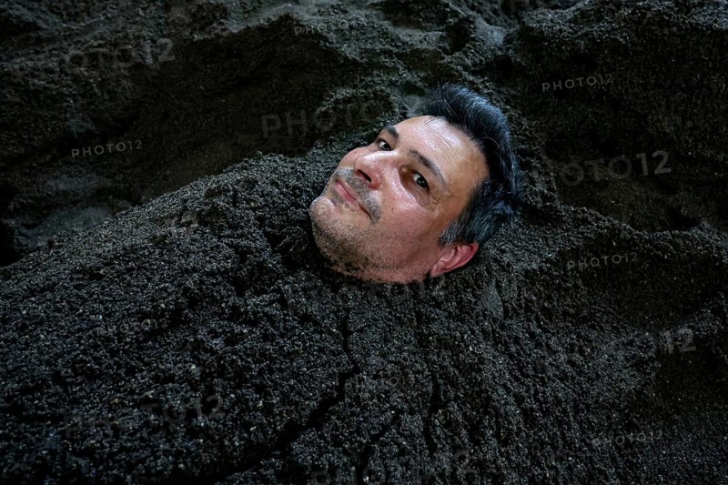 Man buried in sand bath with only his head sticking out, relaxed expression, Beppu, Takegawara Onsen, Japan