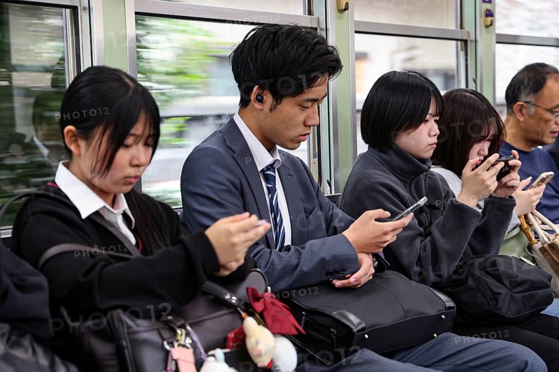 Passengers on a train in Kyoto, including a salaryman, use their smartphones, Arashiyama, Kyoto, Japan