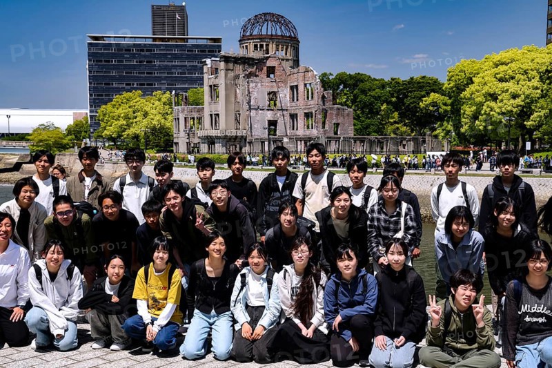 Group of students posing in front of the Hiroshima Memorial in bright sunshine, Hiroshima, Japan