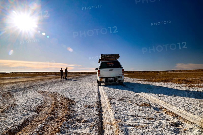 Off-road vehicle drives across a wide salt lake under clear skies, South Australia, Australia