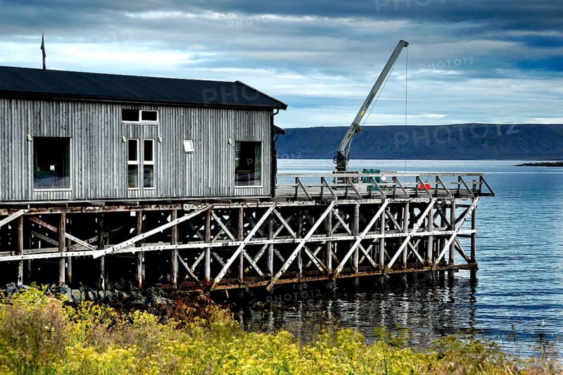 Wooden building on the water in Hamningberg under cloudy sky