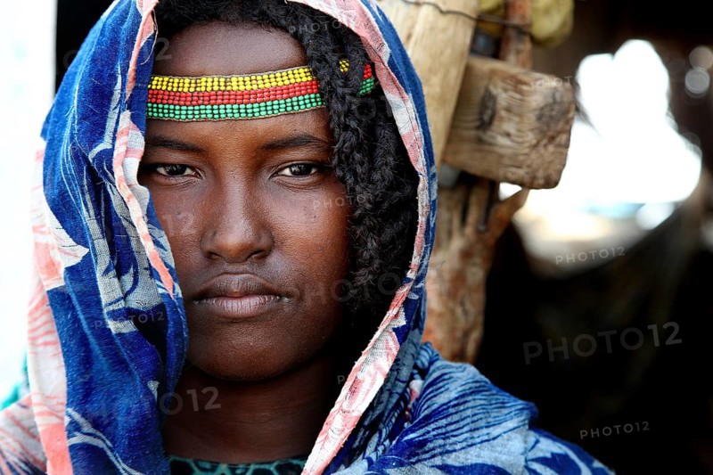 Aishe poses in traditional clothes and colorful accessories in front of Muhammad's hut in Ahmedela, Ahmedela, Ethiopia