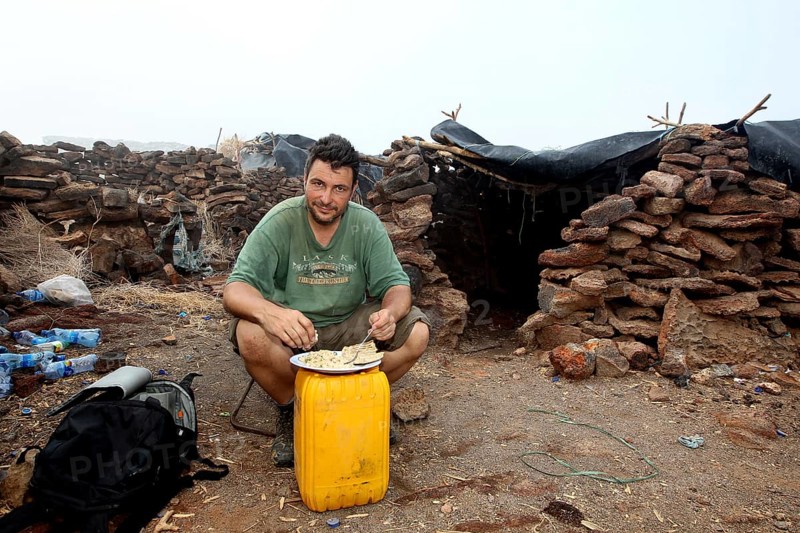 Man sitting in a warehouse of stone huts with minimalistic furniture, zero