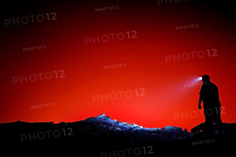 Silhouette of a human with head light against a bright red background, Erta Ale, Ethiopia