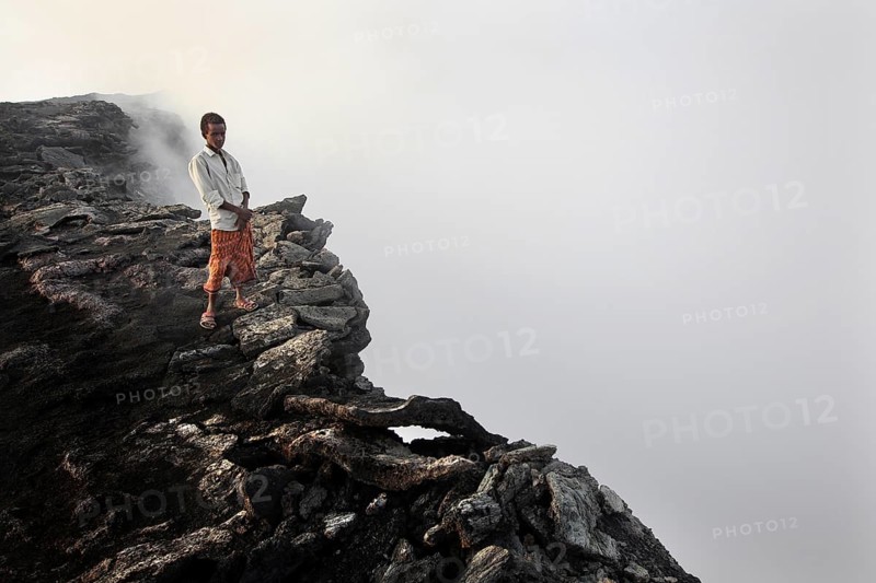 Mountain guide stands at the edge of a smoking crater in a foggy atmosphere, zero