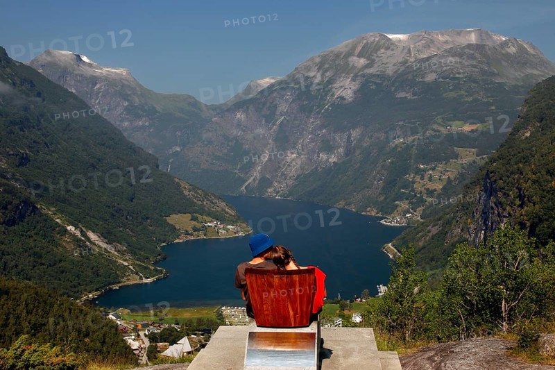 Tourist sits on a red chair and looks at the impressive panorama of Geirangerfjord, Flydalsjuvet, Geirangerfjord, Møre og Romsdal, Norway