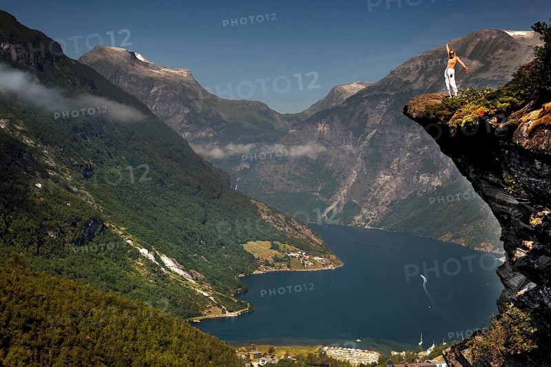 Adventurous tourist stands on cliff and enjoys views of Geirangerfjord, Flydalsjuvet, Geirangerfjord, Møre og Romsdal, Norway