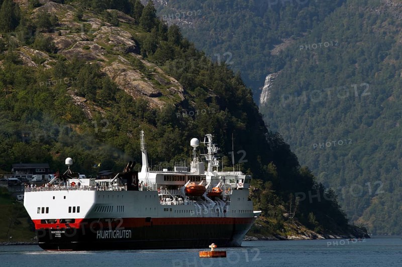 A Hurtigruten ship on calm water off wooded mountain slopes, Geirangerfjord, Norway