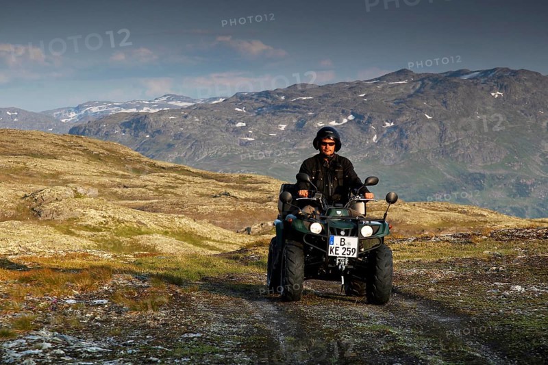 Person driving an ATV through a rugged mountain landscape under cloudy sky, zero
