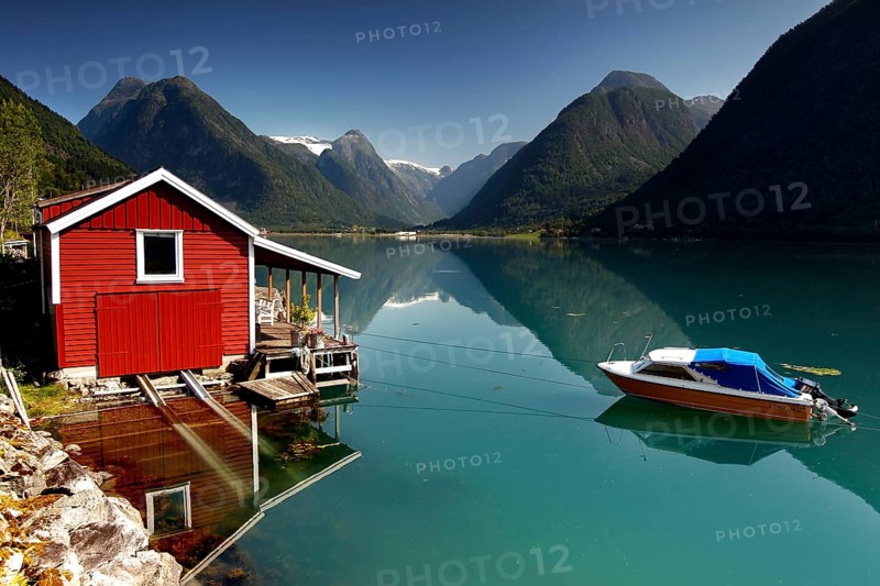 Red hut on the banks of Fjærlandsfjord near Mundal with boat and mountain backdrop, Mundal, Norway