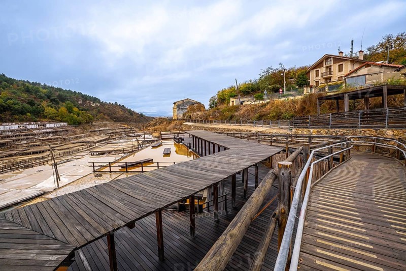 Anana salt valley showcasing traditional salt evaporation ponds, wooden structures, and a historical process of salt production under an overcast sky, with buildings on a hillside