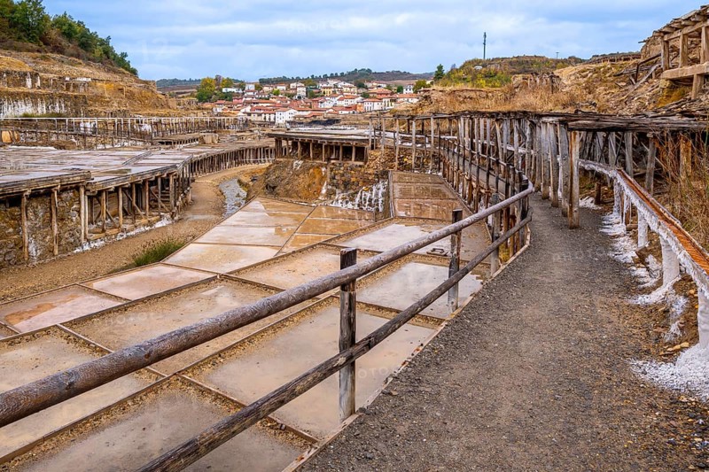 Historic salt valley of anana showing intricate wooden structures and evaporation ponds, creating salt from brine, with a traditional village visible in the background under a cloudy sky